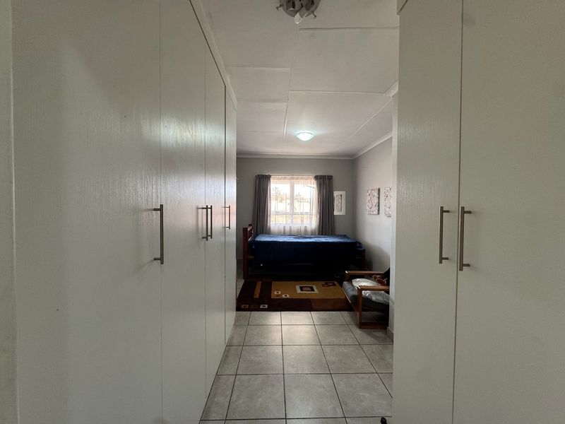 A bedroom featuring extensive built-in cupboards, tiled flooring, and a window allowing natural light, providing a functional living space.