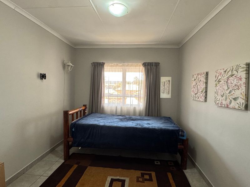 A functional bedroom featuring tiled flooring, neutral wall finishes, and a window providing natural light.