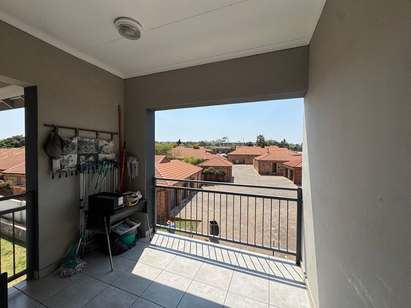 A covered balcony featuring tiled flooring and a metal balustrade, offering an elevated view over the complex grounds.