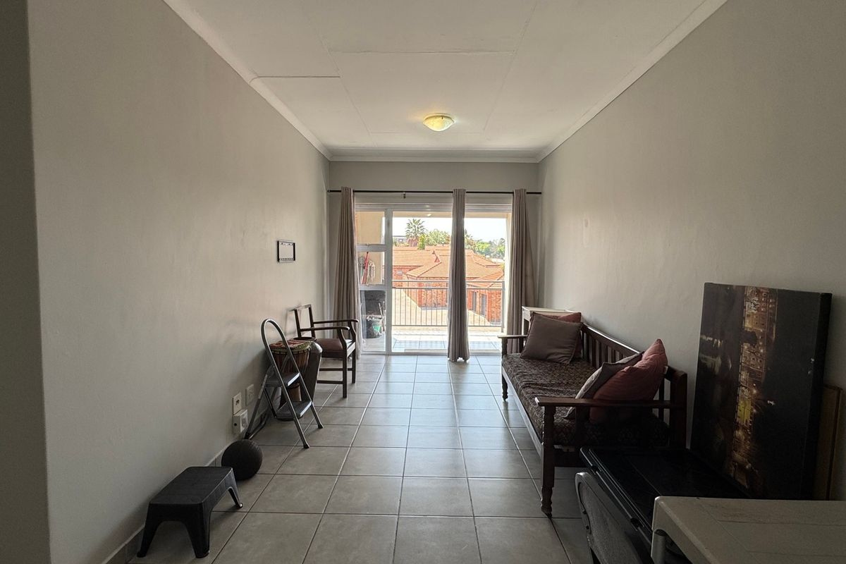A spacious living area featuring neutral walls, tiled flooring, and a sliding glass door providing access to an outdoor balcony.