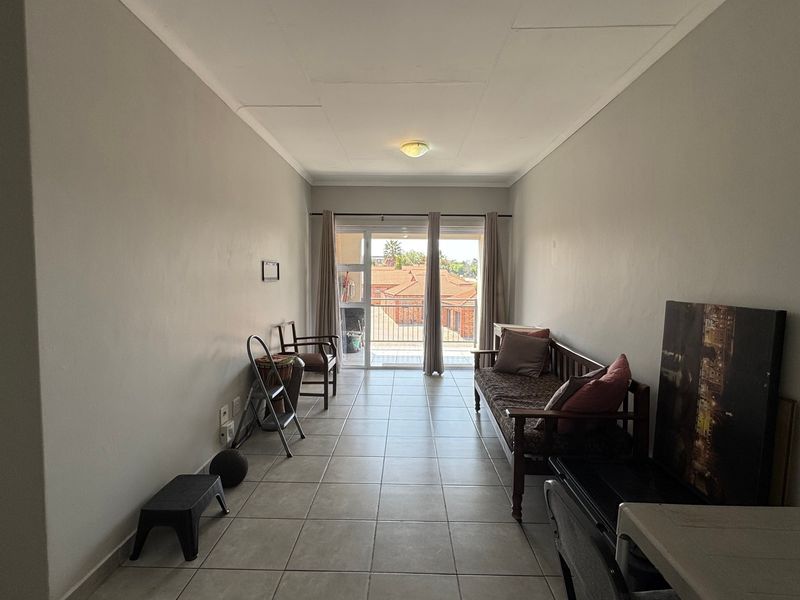 A spacious living area featuring neutral walls, tiled flooring, and a sliding glass door providing access to an outdoor balcony.