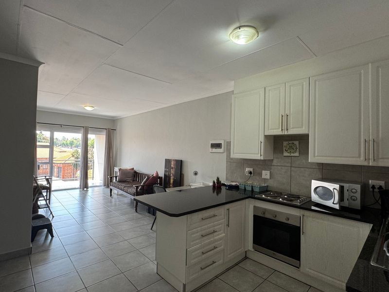 Open-plan living area featuring a modern kitchen with granite countertops, built-in oven and hob, and direct access to a balcony through sliding glass doors.