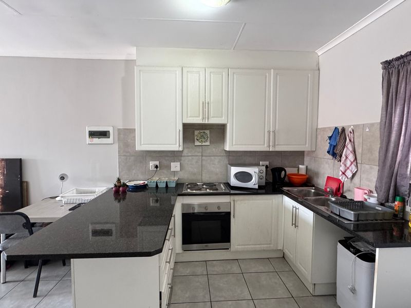 A functional kitchen featuring granite countertops, built-in cabinetry, an electric hob with oven, and a double basin sink with tiled backsplash.
