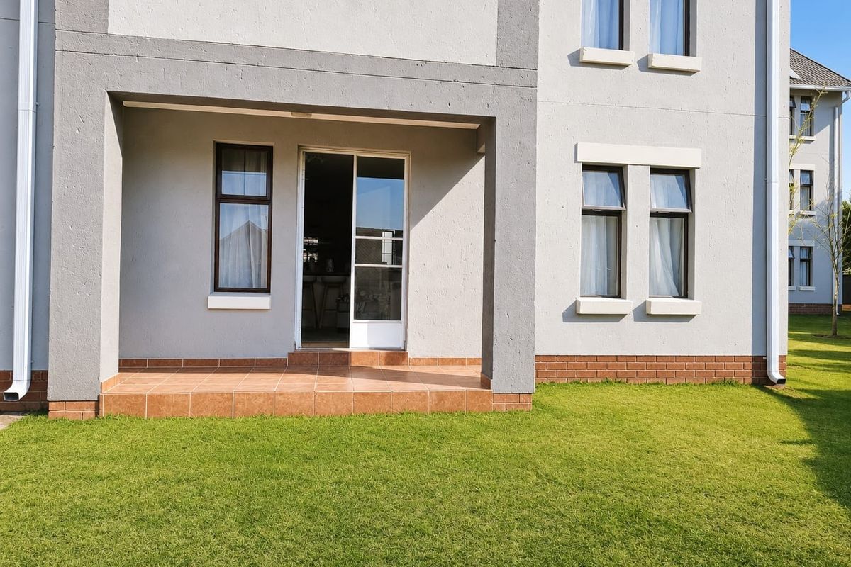 Rear view of the apartment building featuring a tiled patio, sliding glass door access, and well-maintained exterior facade with brick detailing.