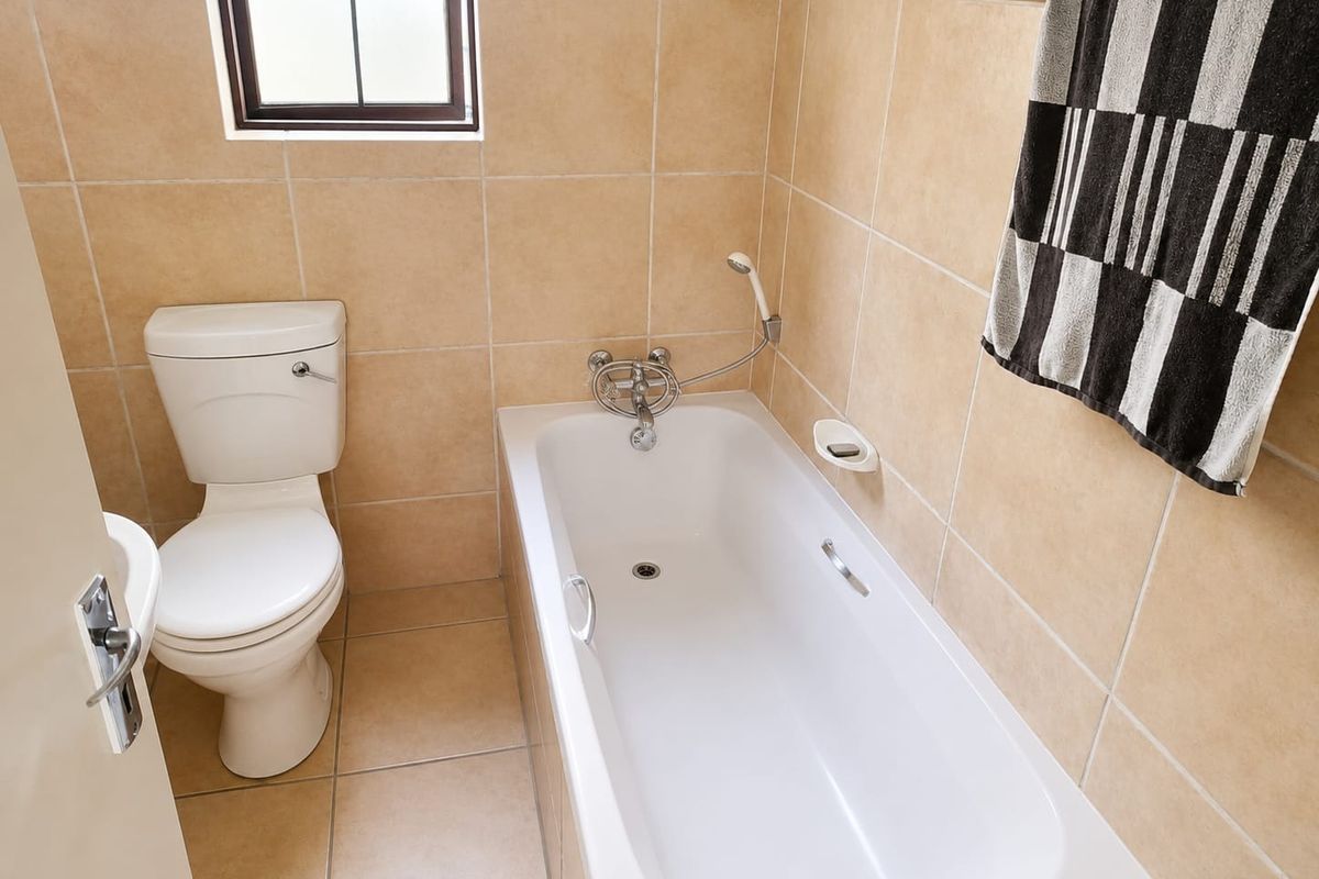 A functional bathroom featuring a standard bathtub with shower mixer, toilet, and neutral wall and floor tiling.