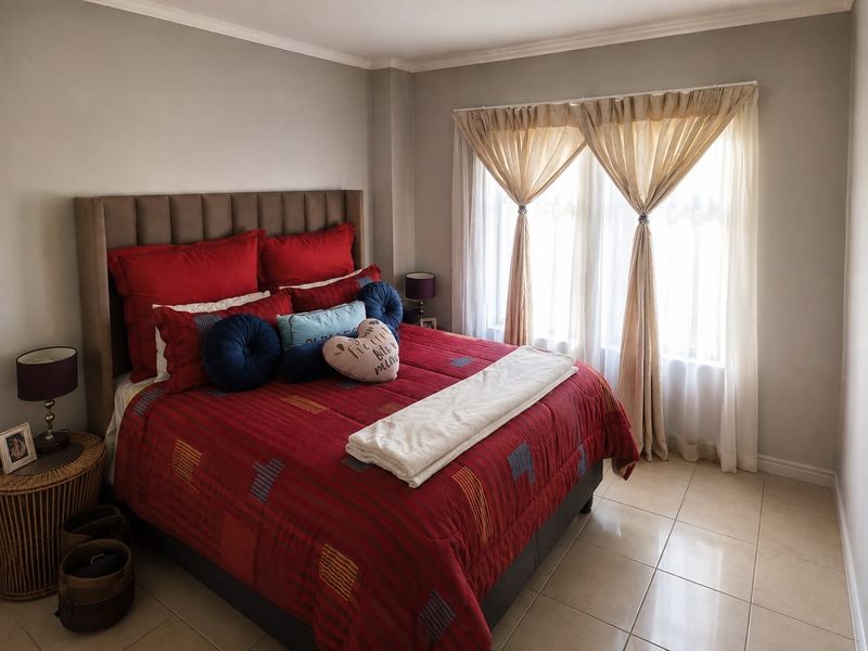 A well-maintained bedroom featuring neutral wall tones, tiled flooring, and a large window allowing for natural light.