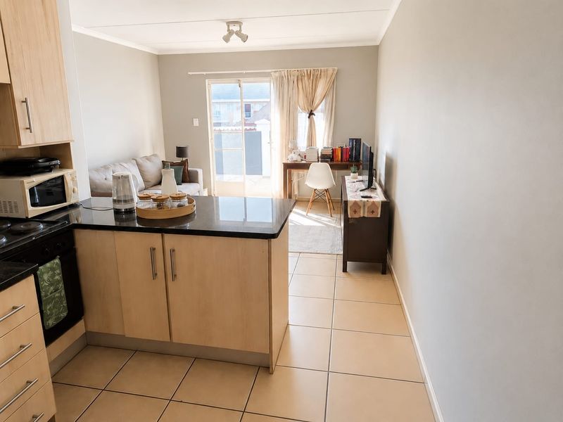 Open-plan living area featuring a modern kitchen with granite countertops, built-in oven, and tiled flooring, leading to a bright living space with sliding door access.