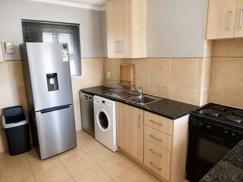 A functional kitchen featuring light wood cabinetry, granite countertops, a stainless steel sink, and a tiled backsplash with integrated electric stove.
