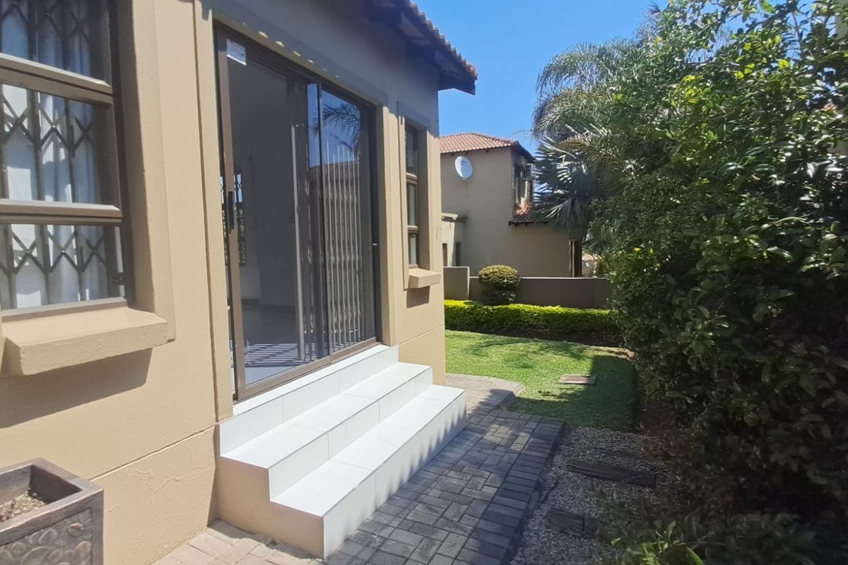 Rear exterior view of the townhouse featuring a paved walkway, small lawn, and sliding glass door access with tiled steps.