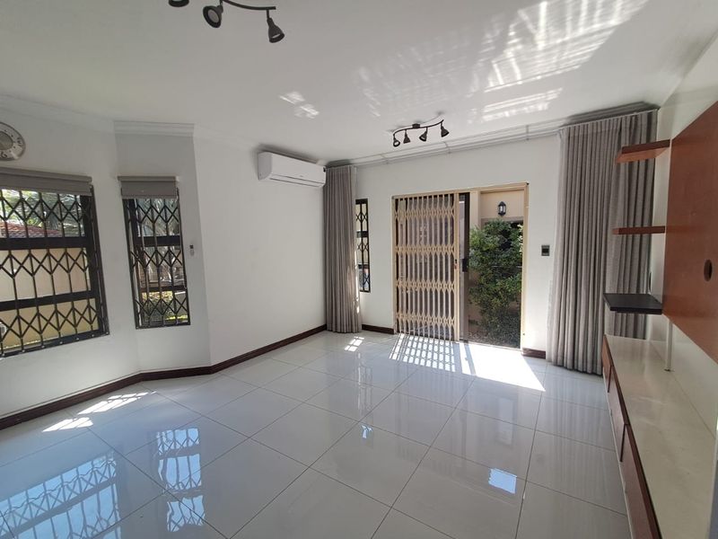A bright, open-plan living area featuring polished tile floors, an air conditioning unit, and direct access to an outdoor space through a sliding door.