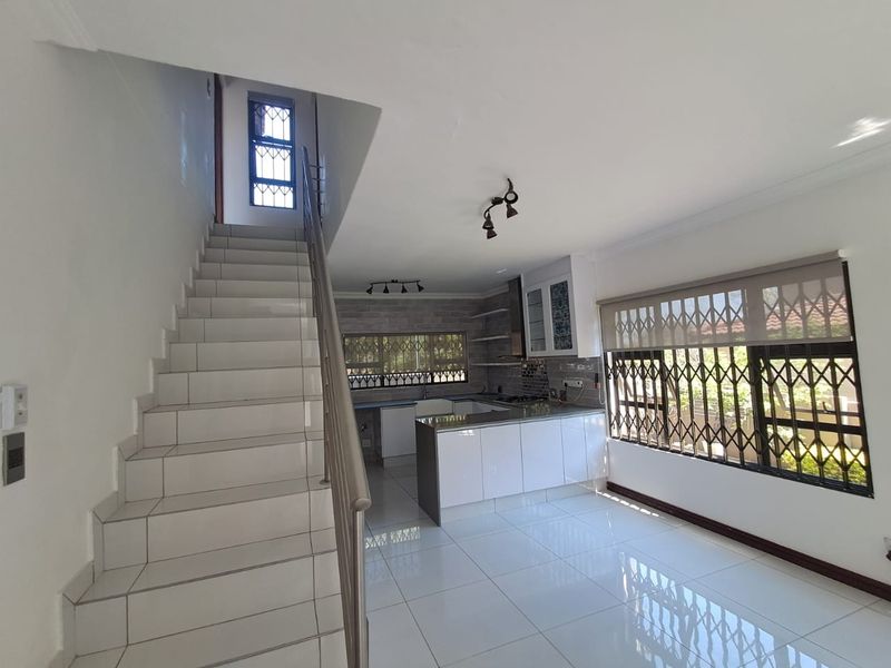 Open-plan kitchen and living area featuring modern white cabinetry, a central island, tiled flooring, and a staircase with a stainless steel handrail.