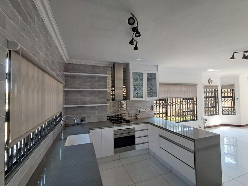 Modern open-plan kitchen featuring sleek white cabinetry, quartz countertops, integrated appliances, and stylish grey subway tile backsplash with ample natural light.
