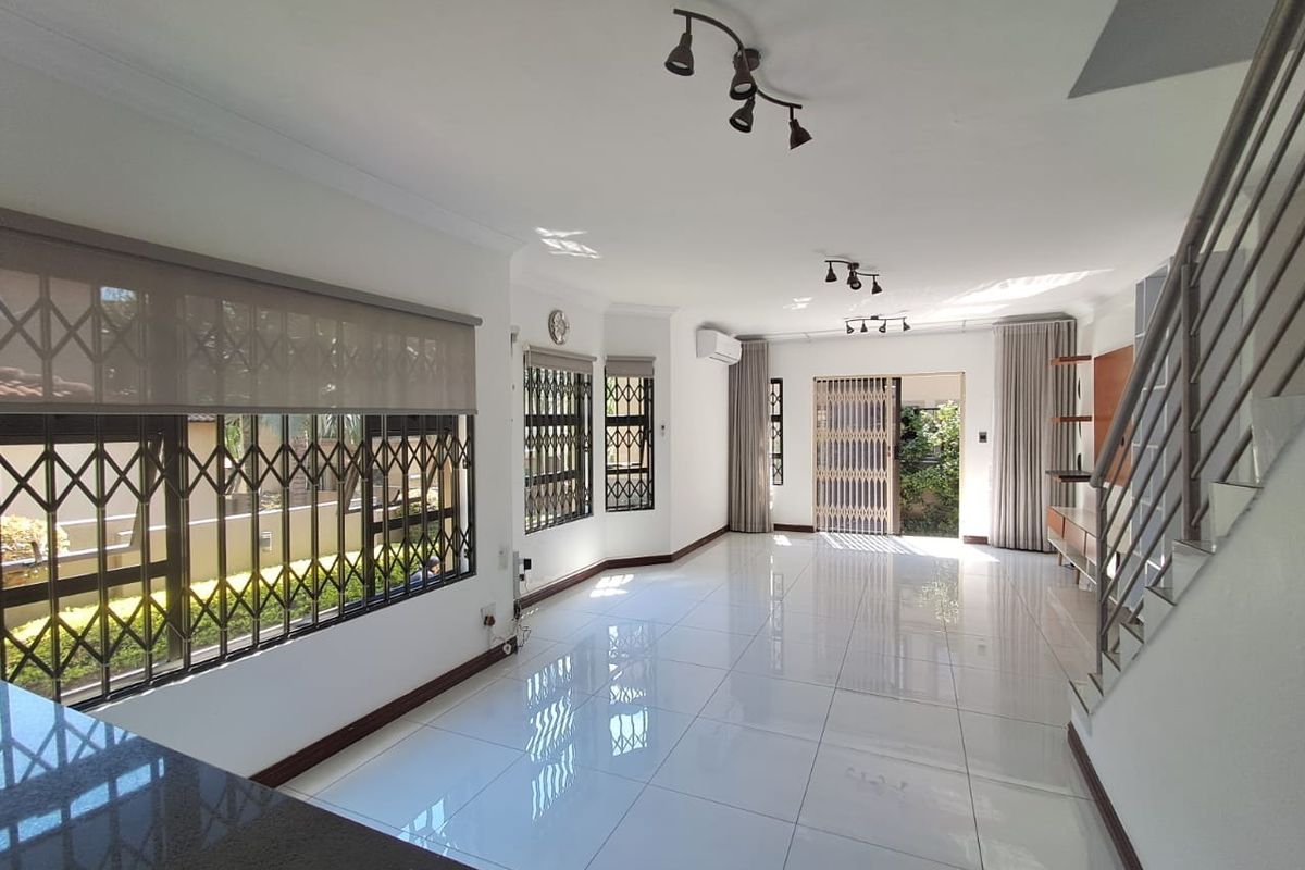 Spacious, light-filled living area featuring polished porcelain tiles, security gates, and a split-system air conditioner, offering a clean and modern open-plan layout.