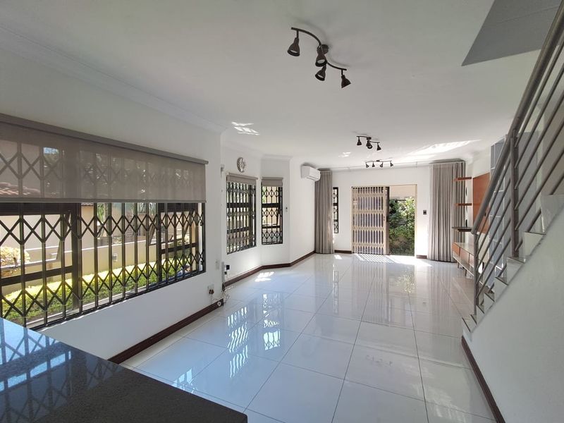 Spacious, light-filled living area featuring polished porcelain tiles, security gates, and a split-system air conditioner, offering a clean and modern open-plan layout.