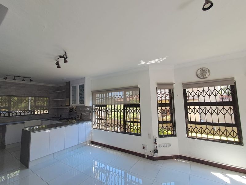 Spacious open-plan kitchen and living area featuring modern white cabinetry, stone countertops, tiled flooring, and secure window treatments.