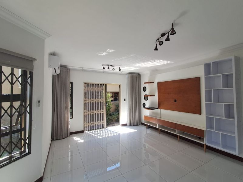 A bright and spacious living room featuring polished tile floors, built-in media cabinetry, shelving, and direct access to an outdoor area through a security gate.
