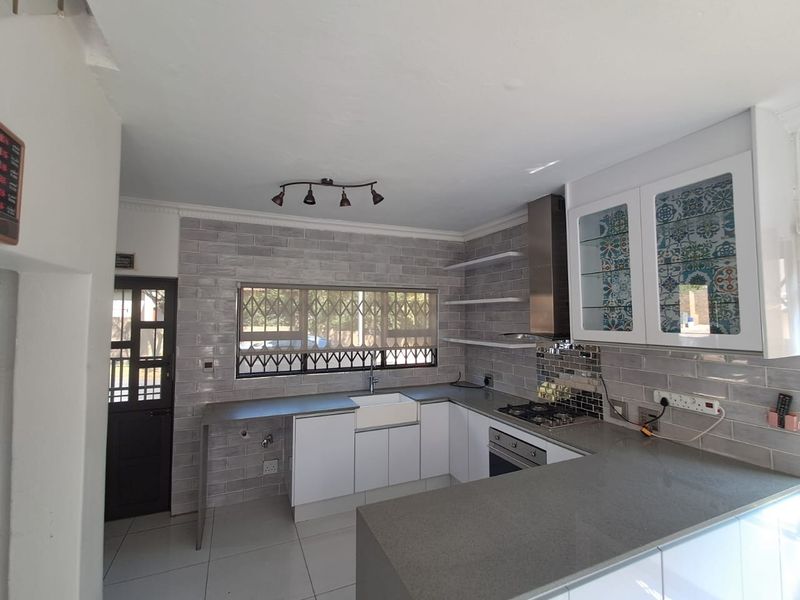 Modern kitchen featuring white cabinetry, grey stone countertops, subway tile backsplash, apron-front sink, and integrated stainless steel appliances.