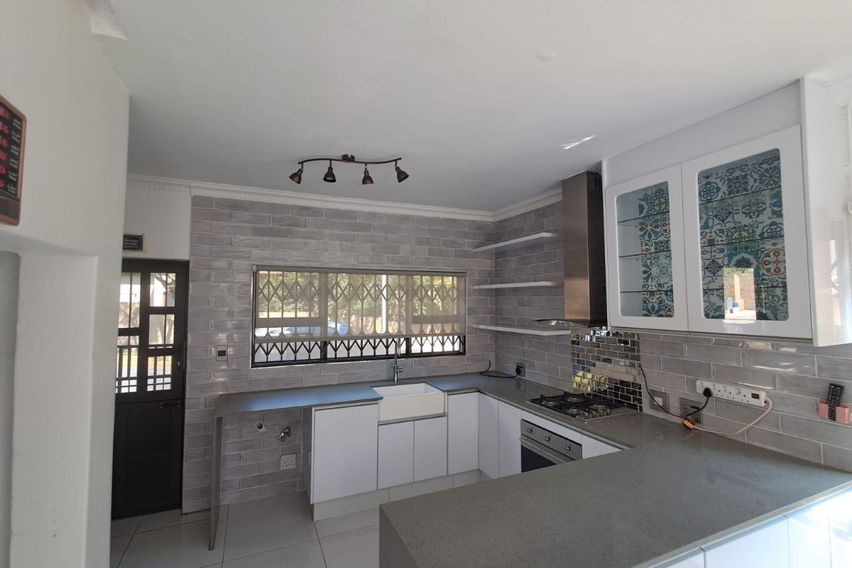 Modern kitchen featuring white cabinetry, grey stone countertops, subway tile backsplash, apron-front sink, and integrated stainless steel appliances.
