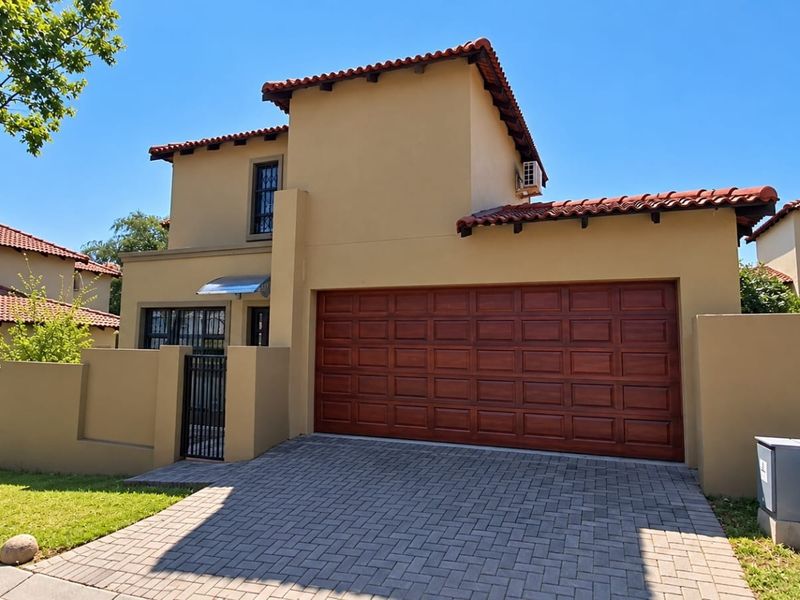 Front elevation of a double-story townhouse featuring a paved driveway, double garage, and secure pedestrian entrance with a tiled roof.