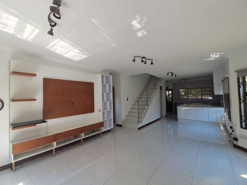 Spacious open-plan living area featuring a modern built-in media unit, tiled flooring, and a sleek kitchen with contemporary cabinetry and stone countertops.