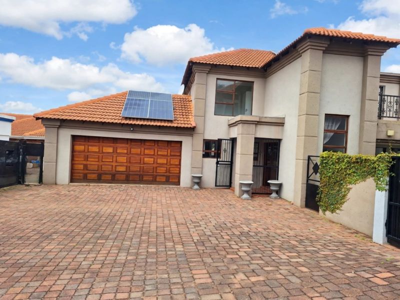 Front elevation of a townhouse featuring a paved driveway, double garage with solar panels on the roof, and secure gated entrance.