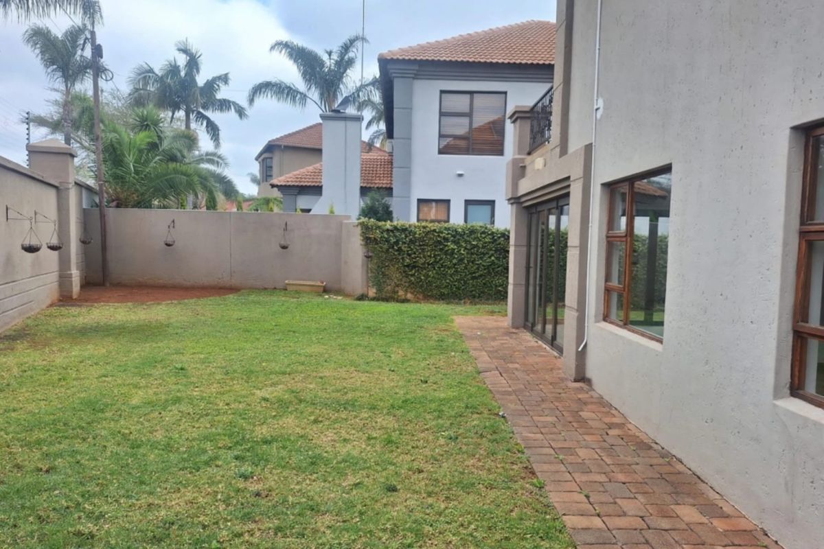 A private rear garden featuring a brick paved walkway, established lawn, and perimeter boundary wall, providing access to the home via sliding glass doors.