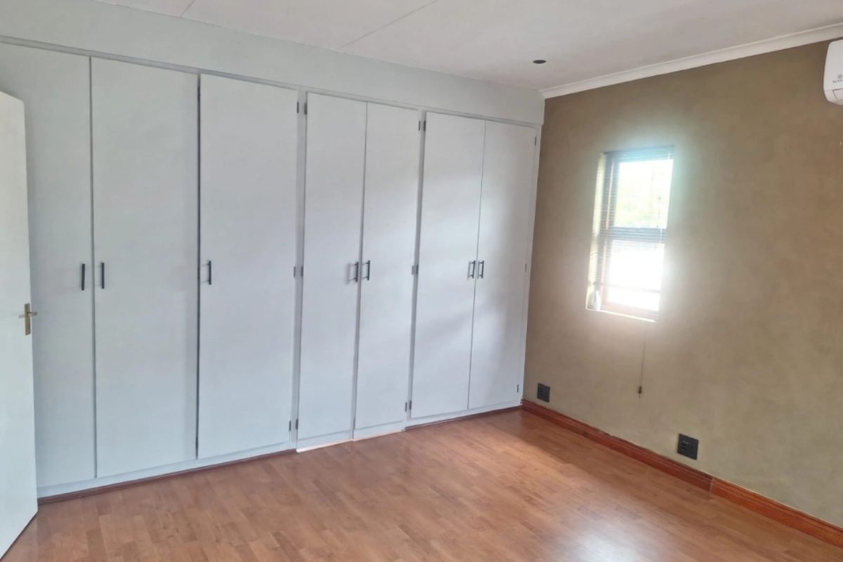 A bright, empty bedroom featuring extensive built-in cupboards, laminate flooring, and a wall-mounted air conditioning unit.