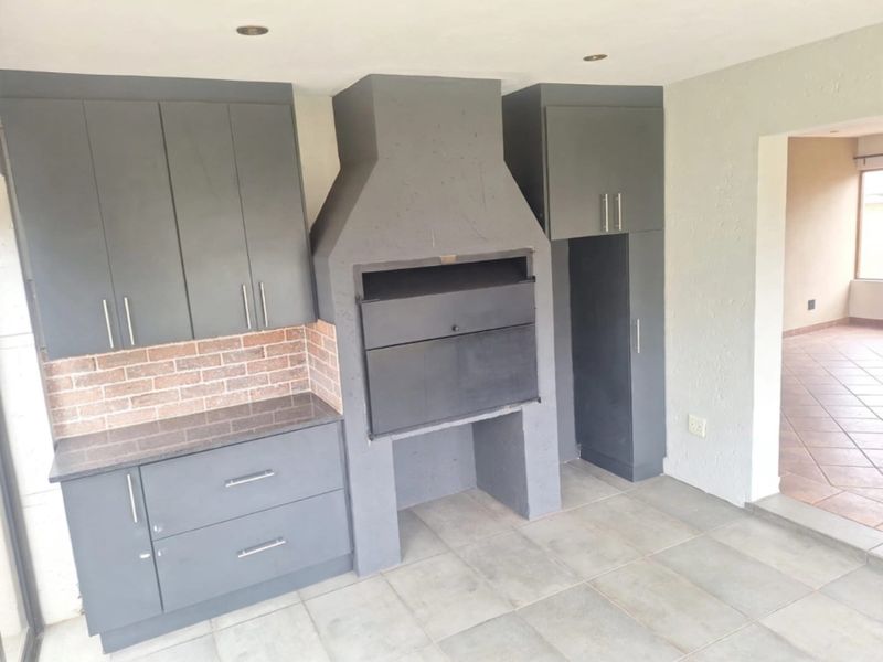 Covered patio area featuring a built-in braai, dark grey cabinetry, granite countertops, and tiled flooring, providing a functional outdoor entertainment space.