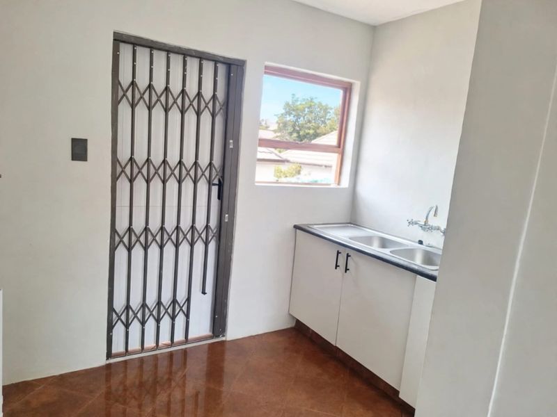 A clean and functional laundry area featuring built-in cabinetry, a stainless steel sink, and a secure exterior door with a metal gate.