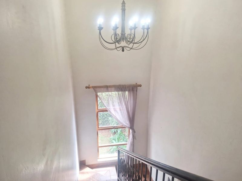A bright staircase landing featuring a wrought iron balustrade, tiled flooring, and a large window overlooking the garden.
