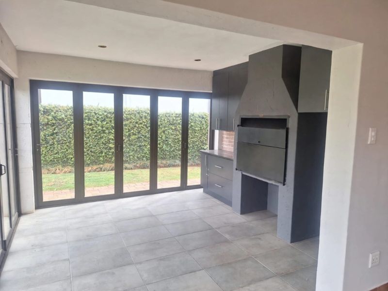 A modern covered patio featuring a built-in braai, sleek cabinetry, and large bi-fold doors opening to the garden.