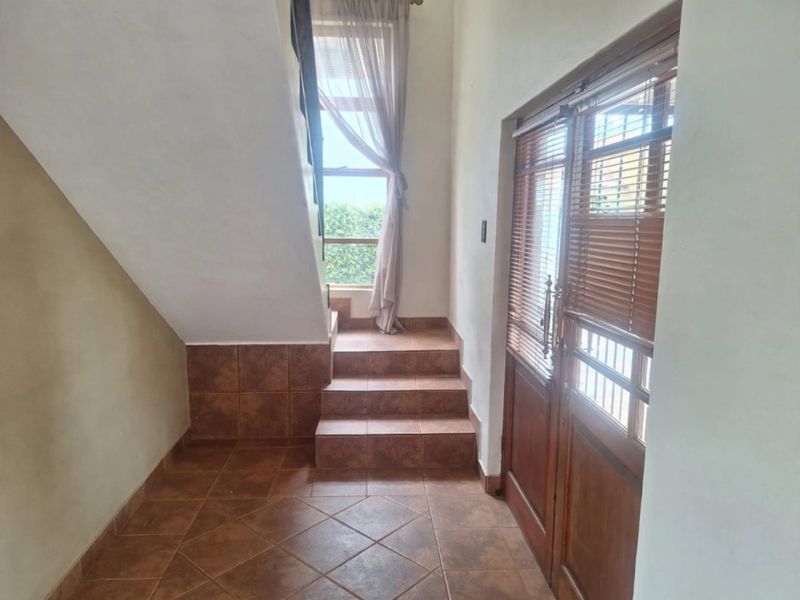 Entrance foyer featuring tiled flooring, a wooden front door with integrated blinds, and a staircase leading to the upper level.