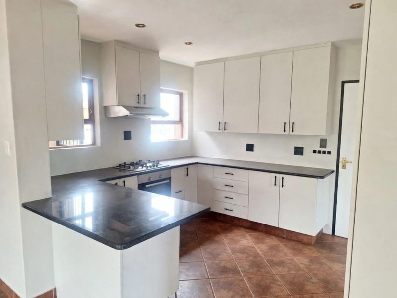 A clean, functional kitchen featuring white cabinetry, dark granite countertops, a gas hob, and an under-counter oven with tiled flooring.