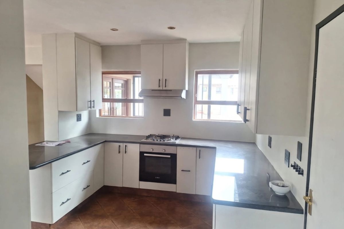 A clean, modern kitchen featuring white cabinetry, dark stone countertops, a gas hob, built-in oven, and tiled flooring.