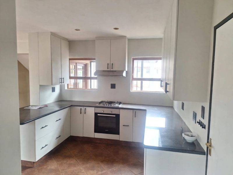 A clean, modern kitchen featuring white cabinetry, dark stone countertops, a gas hob, built-in oven, and tiled flooring.