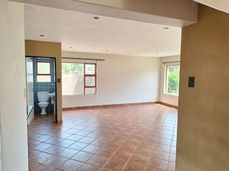 Spacious open-plan living area featuring neutral walls, tiled flooring, recessed lighting, and an adjoining bathroom with modern fixtures.