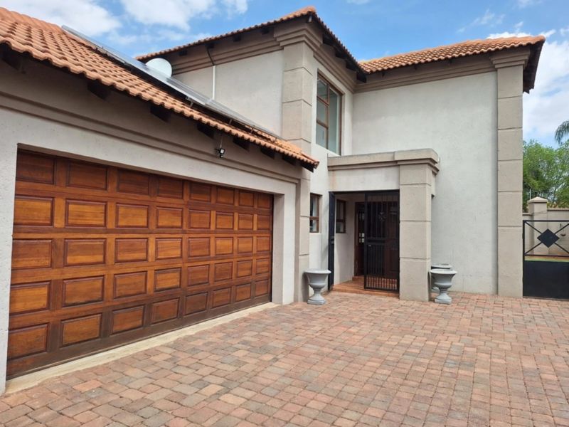 Front elevation of a townhouse featuring a paved driveway, wooden double garage door, and terracotta roof tiles with integrated solar panels.