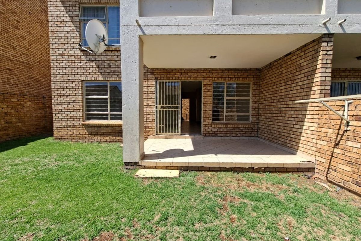Rear view of the apartment featuring a covered tiled patio, brick exterior walls, and a private garden area with a wall-mounted washing line.