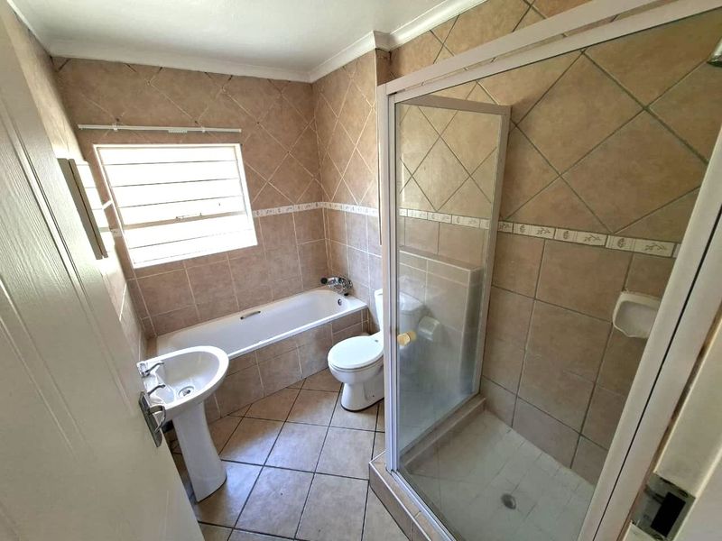 A functional bathroom featuring a pedestal basin, built-in bathtub, and a separate shower enclosure with tiled finishes throughout.