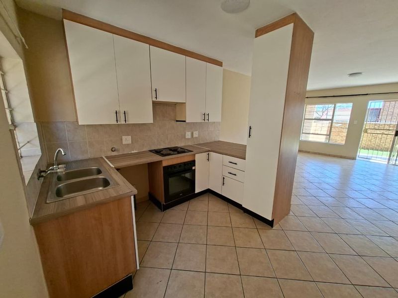 Open-plan kitchen featuring built-in cabinetry, laminate countertops, and integrated oven and hob, flowing into a spacious living area with tiled flooring.