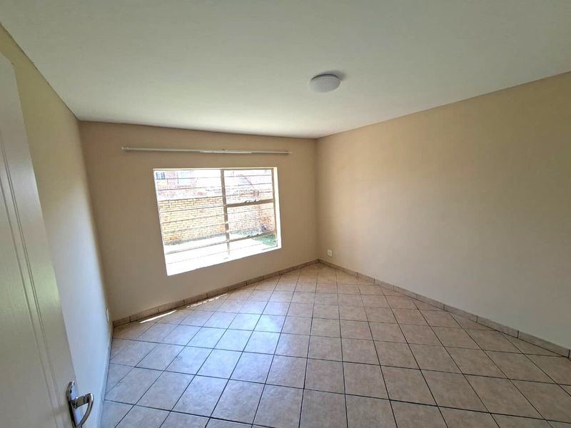 A clean, empty bedroom featuring neutral wall paint, tiled flooring, and a window fitted with security burglar bars.