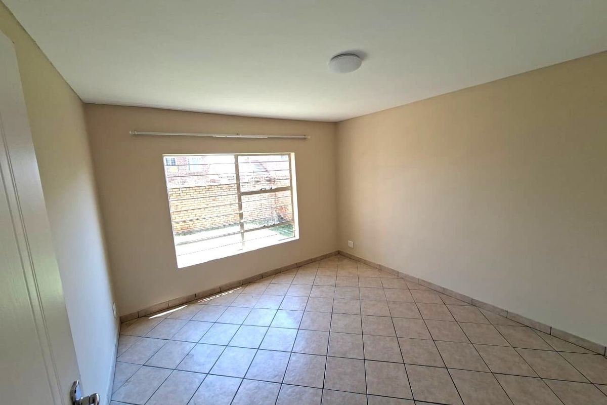 A clean, empty bedroom featuring neutral wall paint, tiled flooring, and a window fitted with security burglar bars.