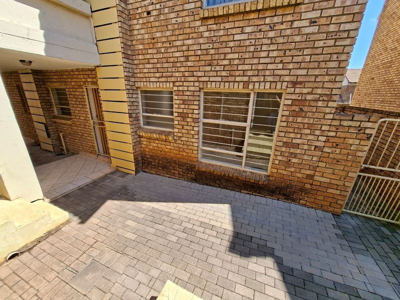 A rear exterior view of the apartment featuring a paved courtyard area and face brick facade with security bars on the windows.