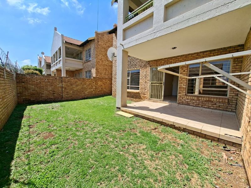 Rear view of the apartment featuring a private garden, a covered tiled patio, and secure brick boundary walls.