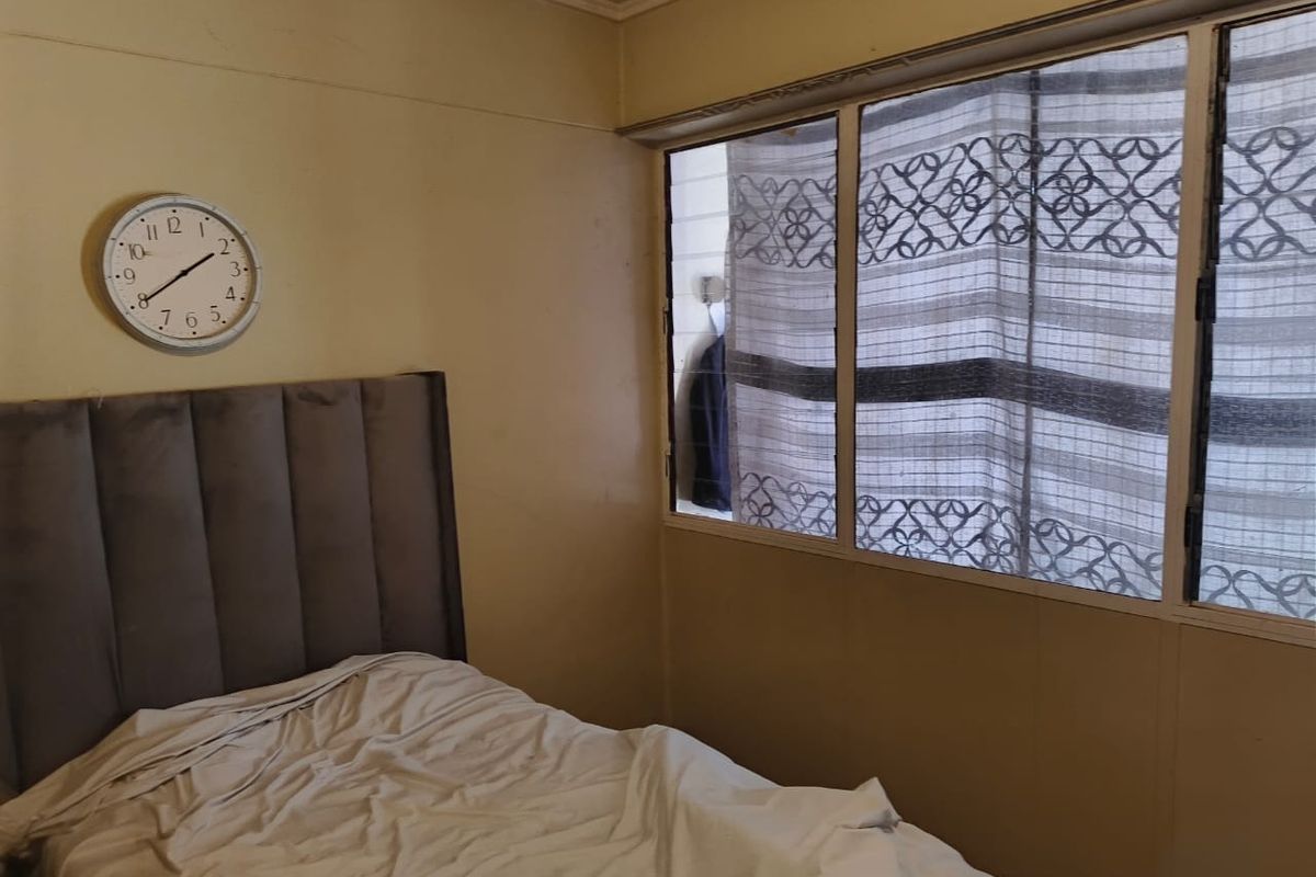 A bedroom featuring aluminium window frames and coved ceiling detailing, requiring cosmetic updates to the wall finishes.