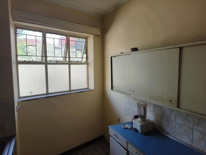 A compact kitchen area featuring dated built-in cabinetry, a tiled backsplash, and a steel-framed window, offering potential for a modern renovation.