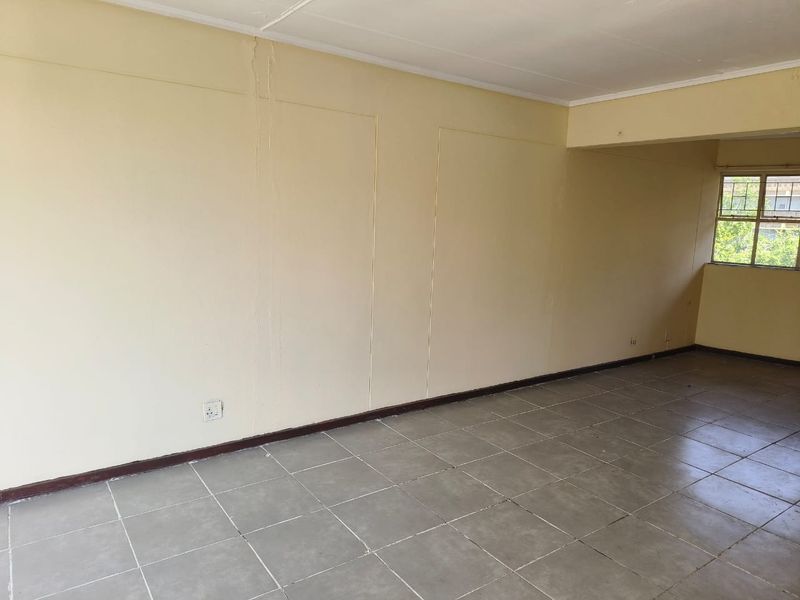 An empty living area featuring tiled flooring and a metal-framed window, requiring cosmetic updates to address wall imperfections and dated finishes.