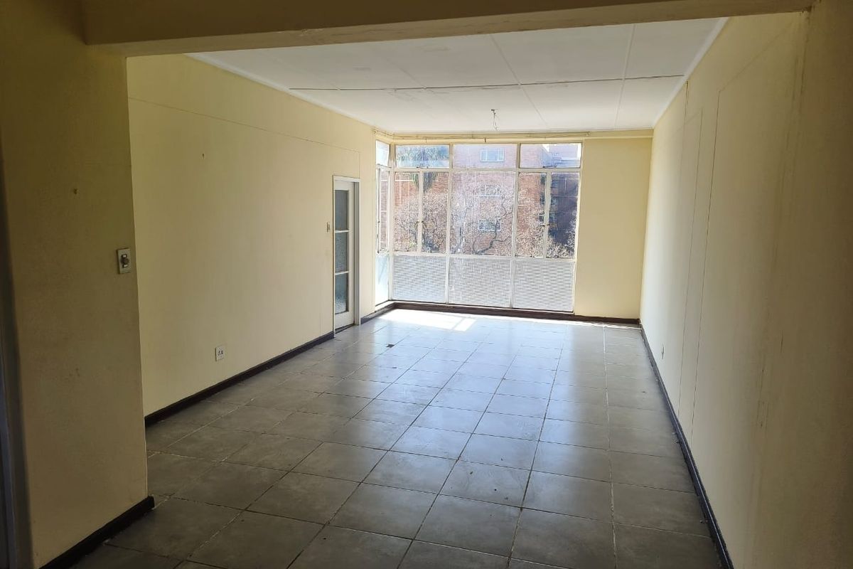 An empty, open-plan living area featuring tiled flooring, large windows providing natural light, and a glass door leading to an exterior space.