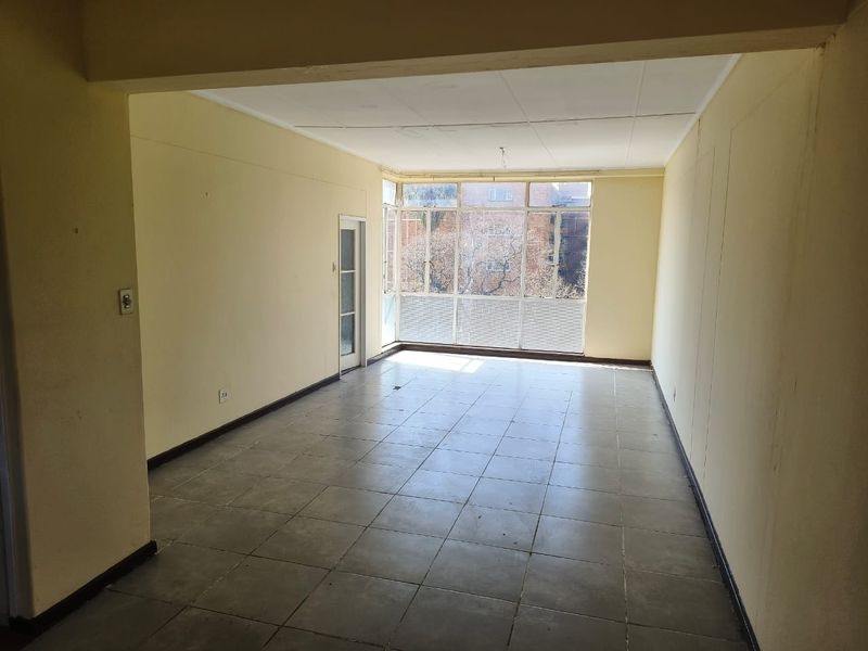 An empty, open-plan living area featuring tiled flooring, large windows providing natural light, and a glass door leading to an exterior space.