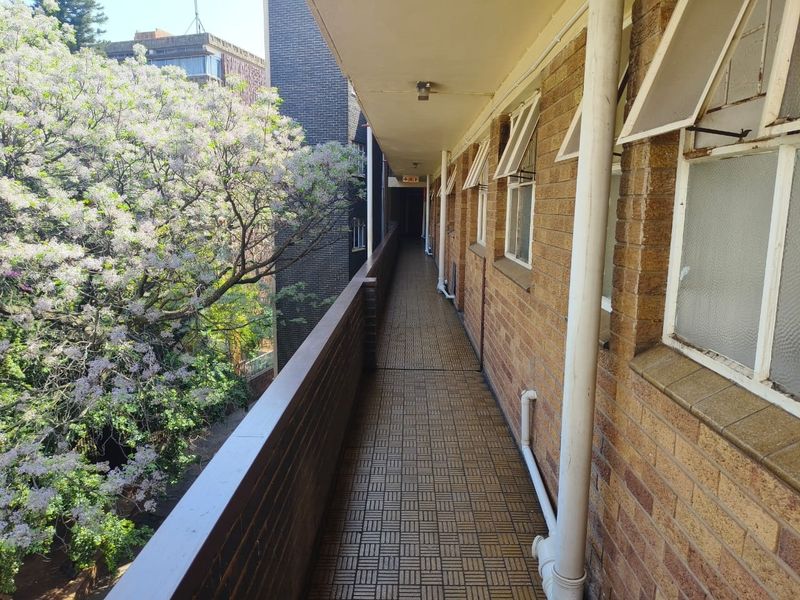 An exterior apartment balcony featuring brick walls, tiled flooring, and a metal balustrade, overlooking mature trees.